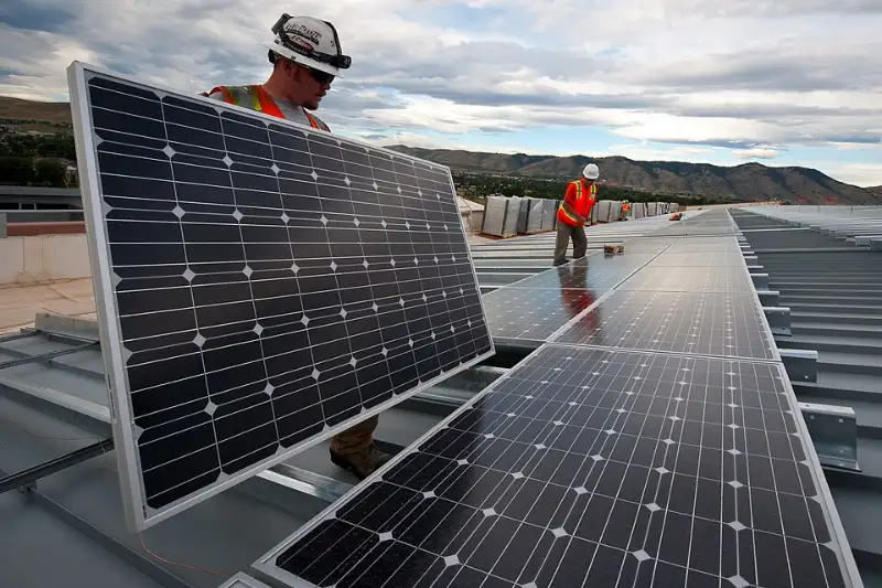 Installers in hard hats mounting solar modules on a commercial roof