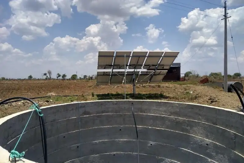 Solar panels powering a water pump beside an open well on farmland in India