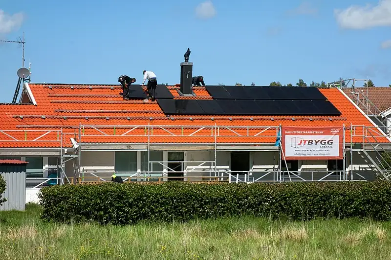 Installers fitting black solar panels on the tiled roof of a family home