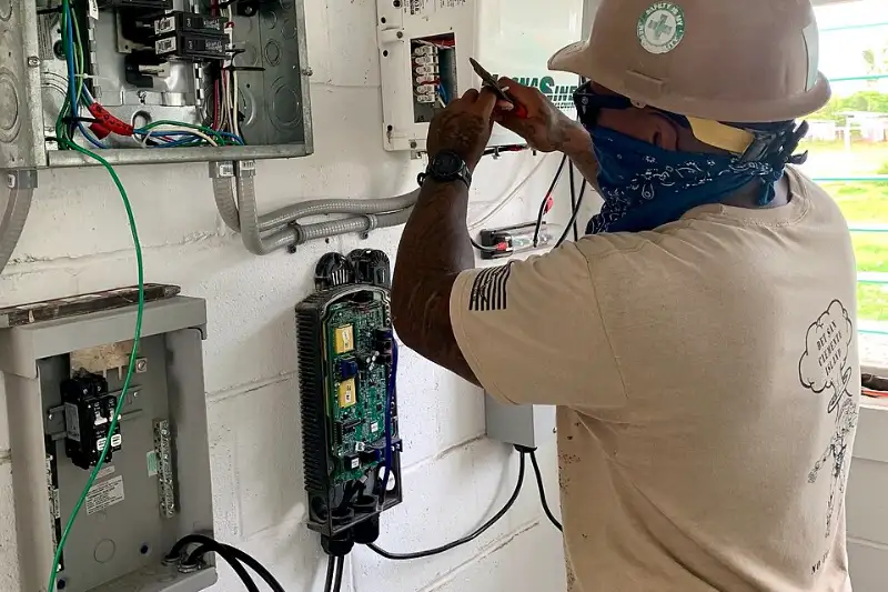 Electrician in a hard hat servicing the wiring and controller of a solar power system